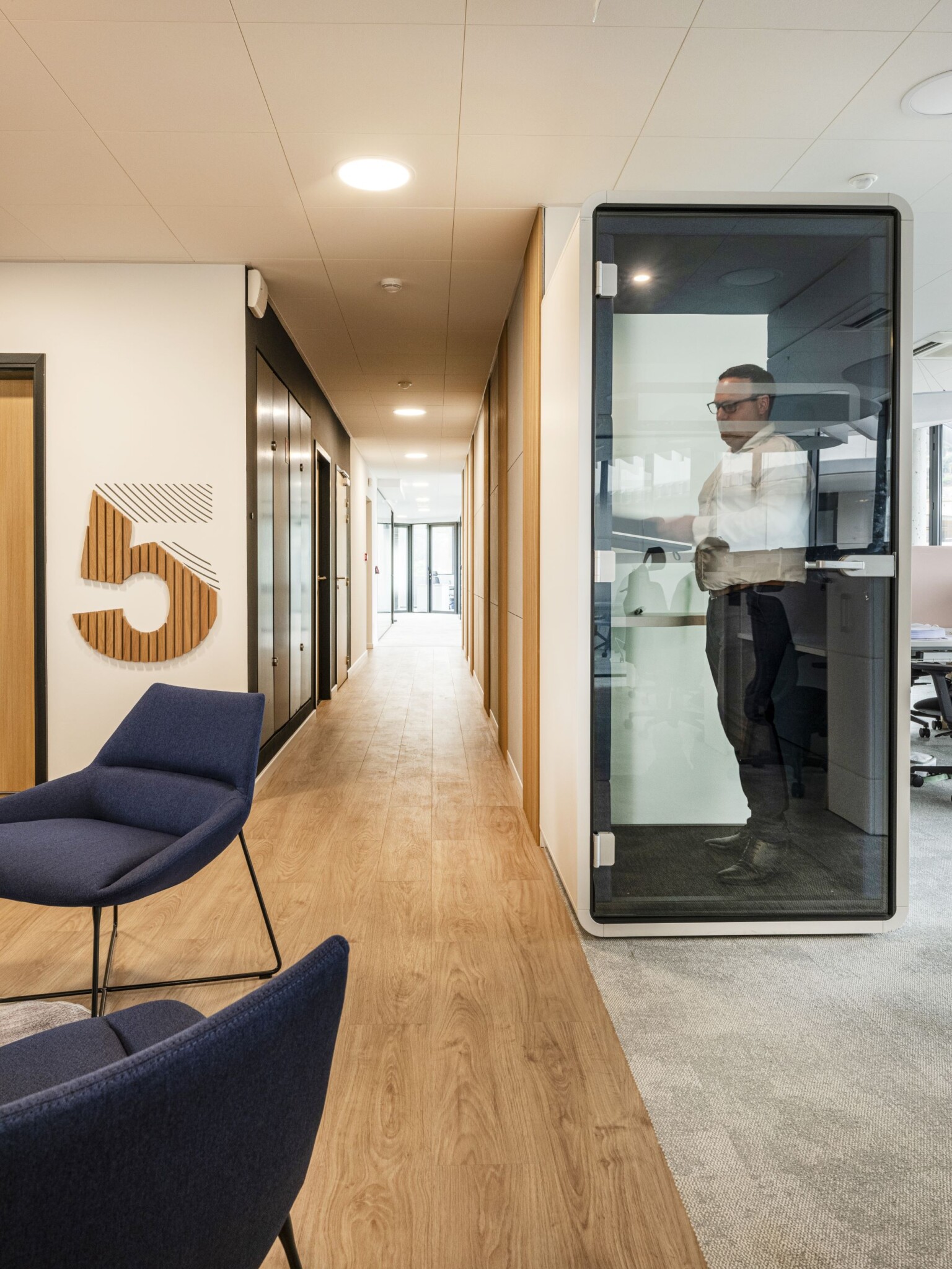 Couloir de bureaux avec cabine acoustique et fauteuils bleus